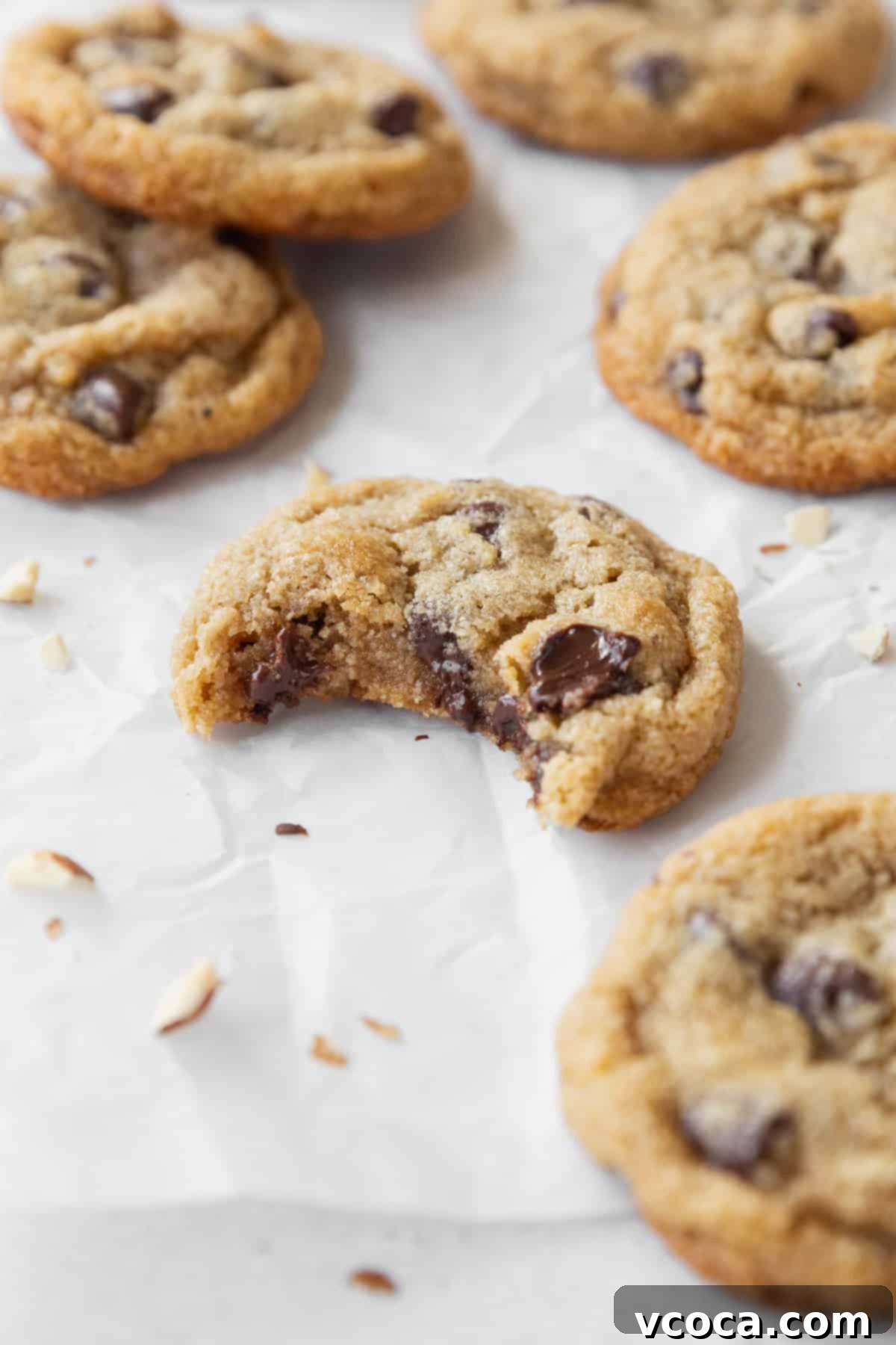 Irresistible Almond Flour Chocolate Chip Cookies 2 A perfectly baked, slightly bitten almond flour chocolate chip cookie resting on a white surface, surrounded by more golden-brown cookies ready to be devoured.