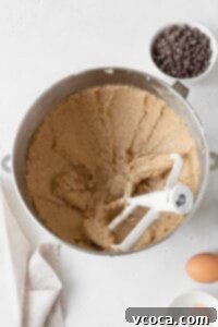 Creamed butter and sugar in the bowl of a stand mixer with an egg on the side and a bowl of chocolate chips in the background, ready for the next step.
