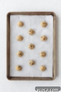 Uniform cookie dough balls, scooped onto a parchment paper lined baking sheet, ready for baking.