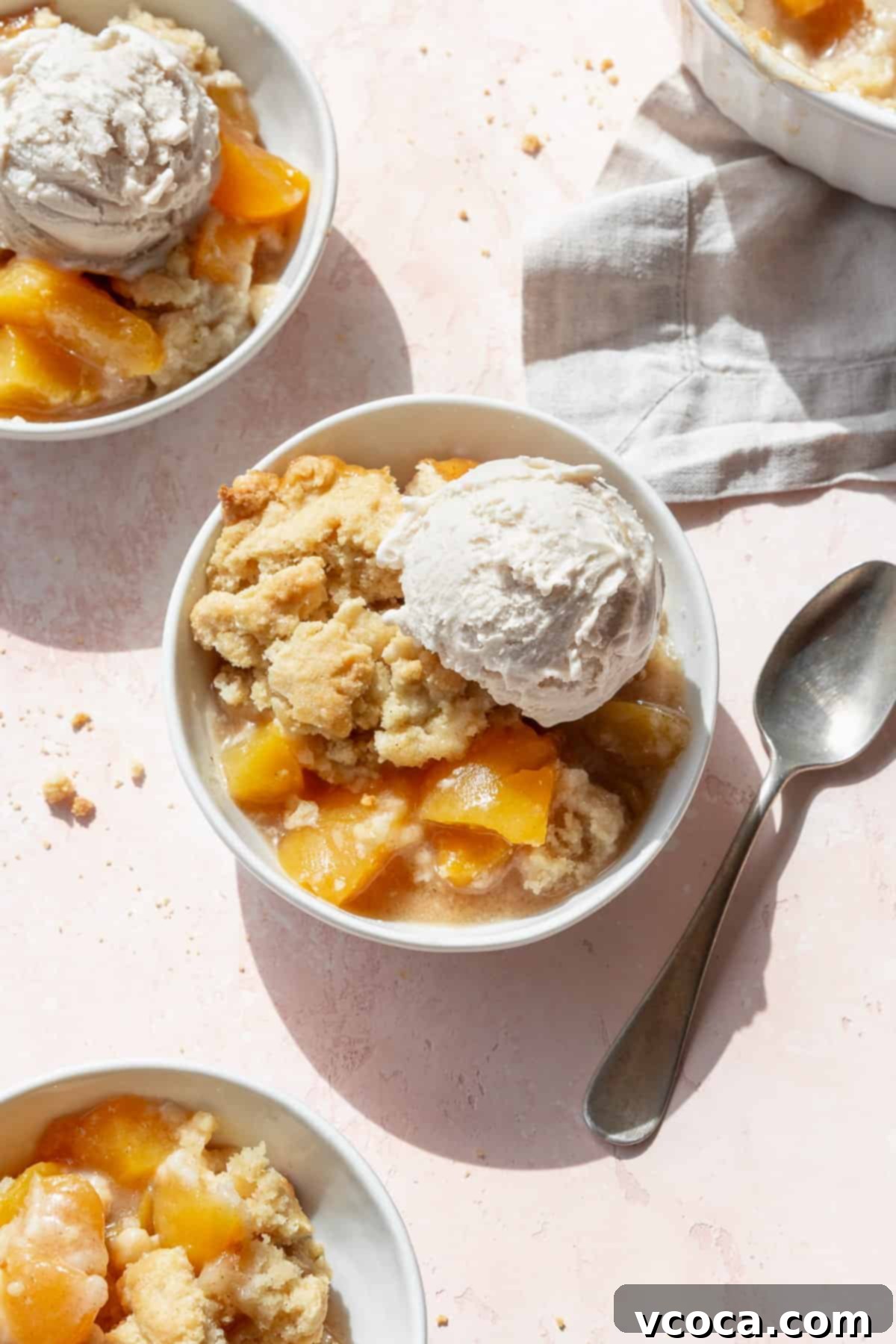 Homemade Peach Cobbler 2 Overhead shot of peach cobbler with canned peaches in three white bowls with scoops of vanilla ice cream.