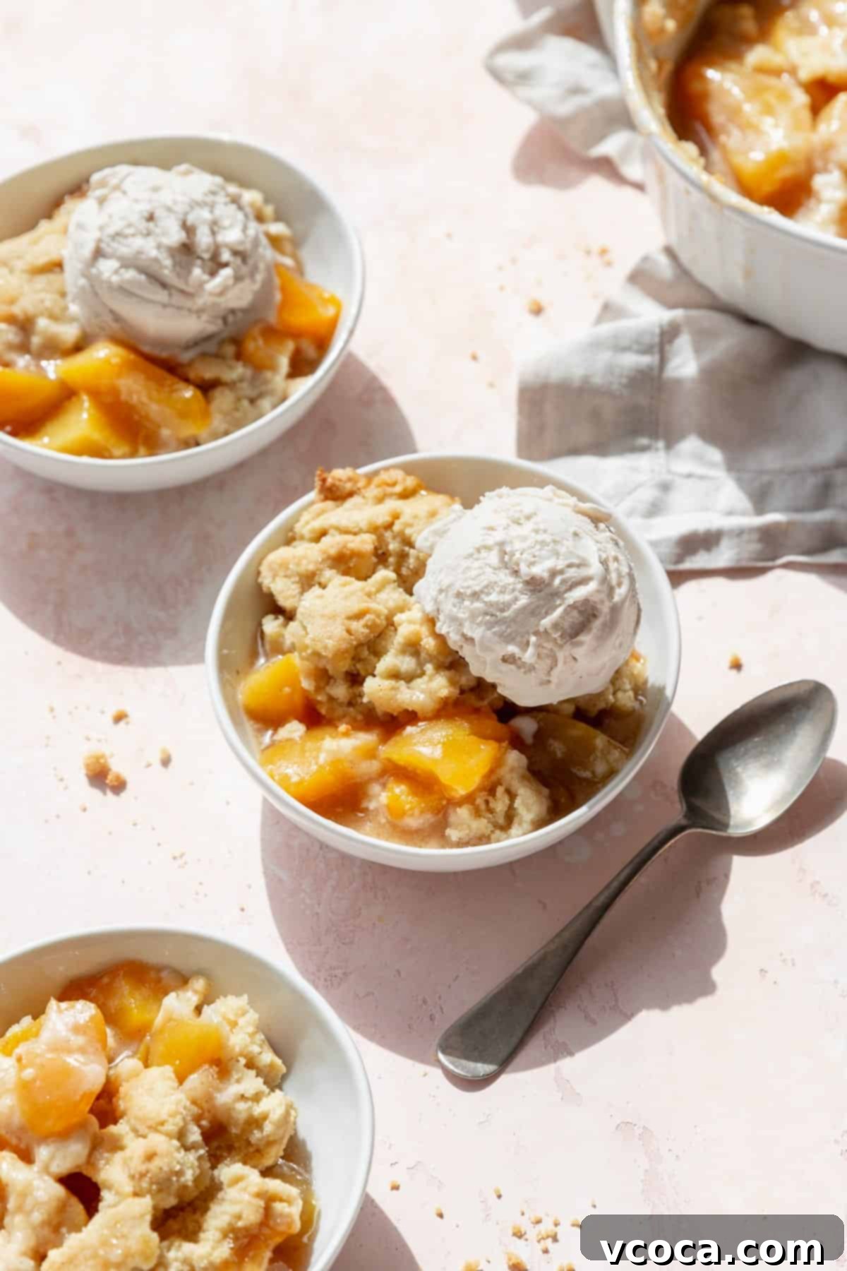 Homemade Peach Cobbler 5 Peach cobbler with a scoop of ice cream in a dessert bowl with a spoon next to it, and more bowls scattered around.