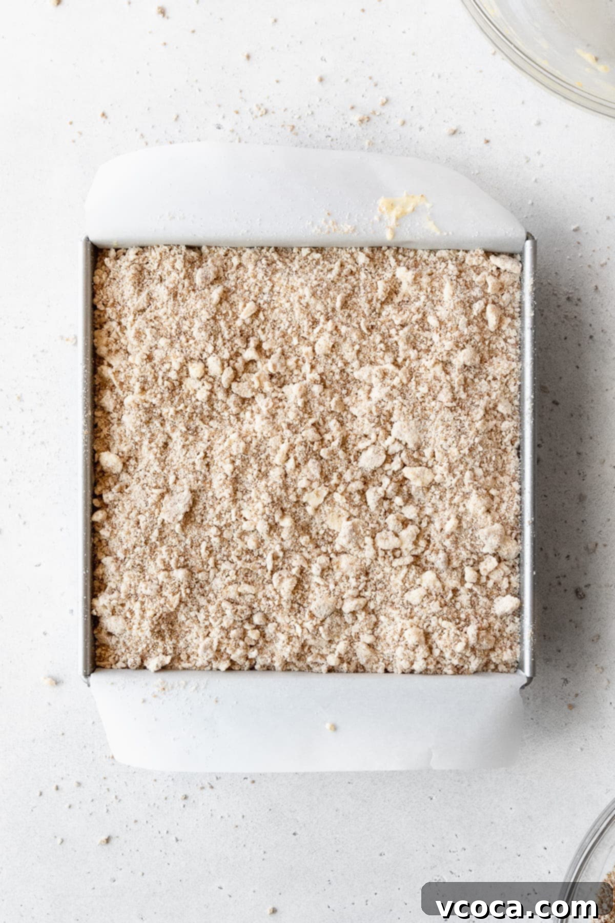 Blueberry Coffee Cake 15 Coffee cake batter topped with crumb topping in a square pan, ready to be baked in the oven.