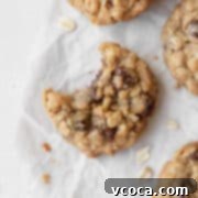 Delicious Gluten-Free Oatmeal Cookies 5 A beautifully baked gluten-free oatmeal cookie with visible chocolate chips, freshly broken to reveal its soft, chewy interior. It sits on a white surface, surrounded by more cookies.