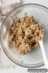 Gluten-free oatmeal cookie dough, featuring chocolate chips, resting in a glass bowl with a white silicone spatula, ready for chilling.