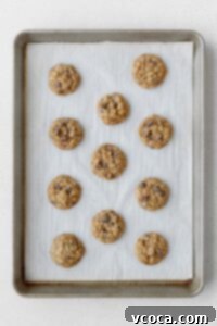 Freshly baked gluten-free oatmeal cookies cooling on a baking sheet lined with parchment paper, showcasing their golden edges and soft centers.