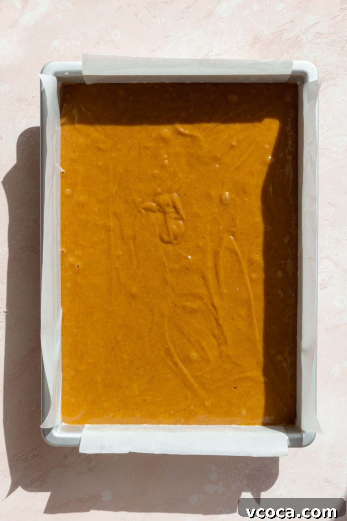 Spiced Pumpkin Squares 9 Pumpkin bar batter smoothly poured into a parchment-lined baking pan, ready for the oven.
