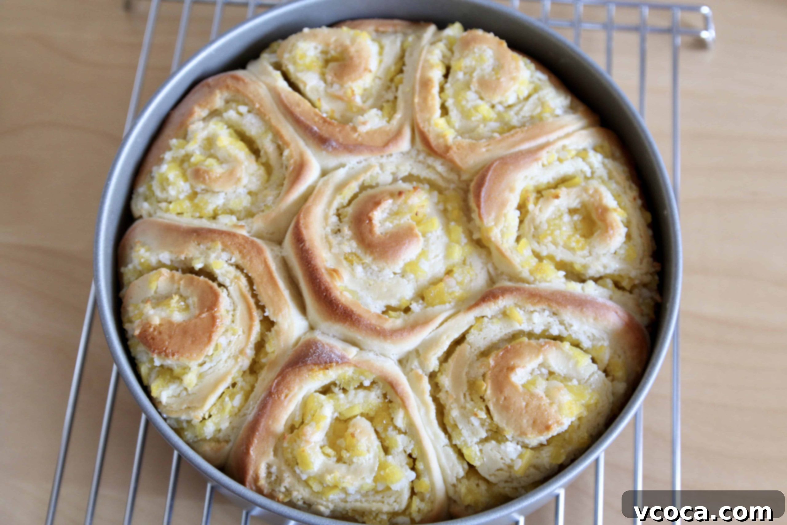 Tropical Piña Colada Swirls 8 Freshly baked pineapple sweet rolls in a round pan, cooling on a wire rack, with frosting drizzled over them