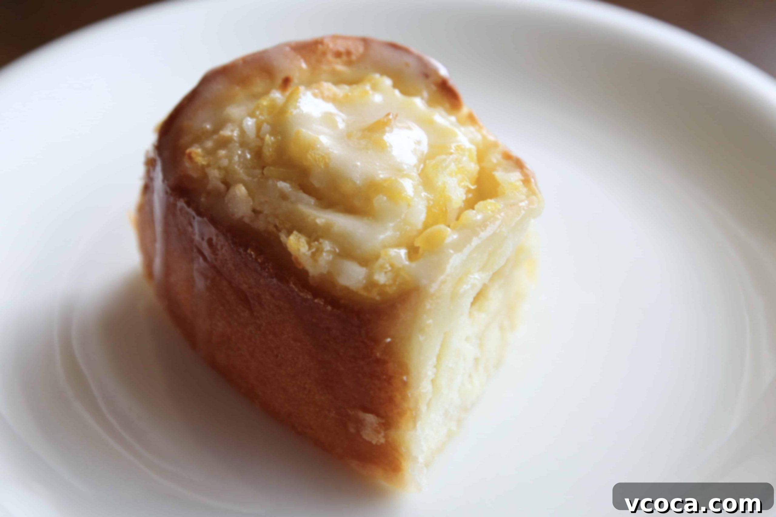 Tropical Piña Colada Swirls 9 A single Piña Colada roll on a white plate, showcasing its fluffy texture and generous frosting