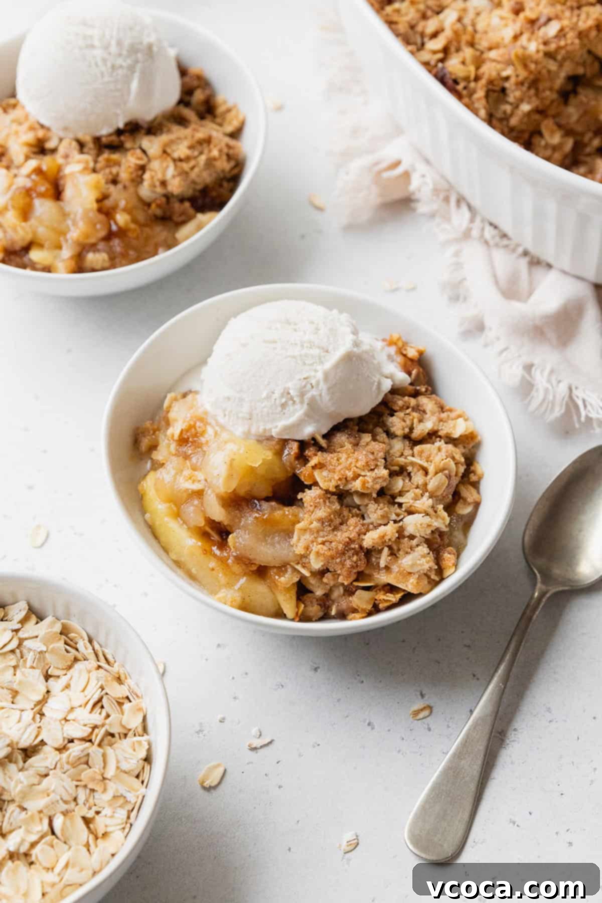 Comforting Gluten-Free Apple Crisp 2 Gluten-free apple crisp with vanilla ice cream in a small white bowl next to a spoon with more bowls placed nearby.
