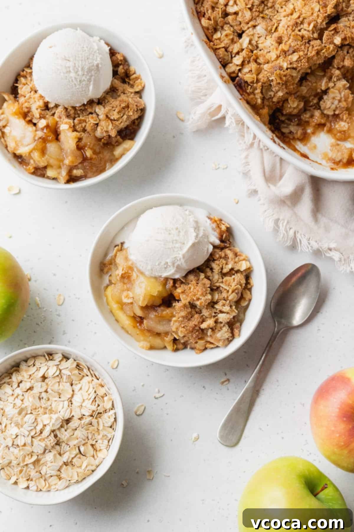 Comforting Gluten-Free Apple Crisp 4 Two bowls of gluten free apple crisp with vanilla ice cream, and a baking dish of more apple crisp placed nearby.