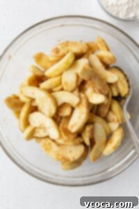 Sliced apples tossed with spices in a glass bowl.
