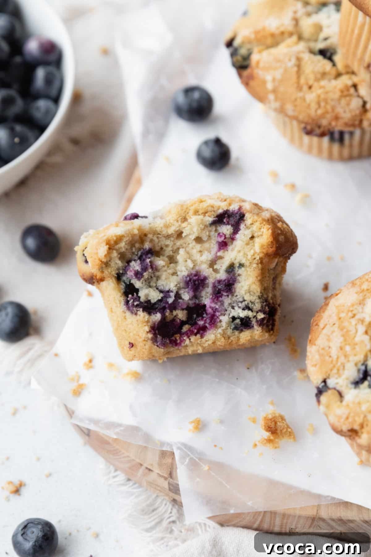 Guilt-Free Blueberry Muffins 2 A bitten blueberry muffin on its side, showing specks of juicy blueberries inside.