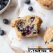 Guilt-Free Blueberry Muffins 4 A bitten gluten free blueberry muffin laying on its side on parchment paper.