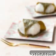 Sakura Mochi 3 Sakura mochi wrapped in a cherry blossom leaf on a square pink plate with a gold fork laying in front. A delicious Japanese spring dessert.