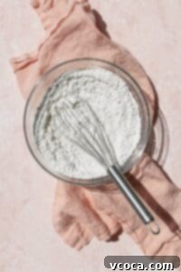 A glass bowl of dry ingredients whisked together on a pink surface.
