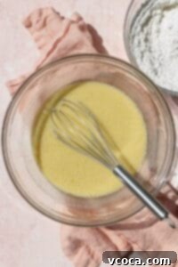 A glass bowl with the wet ingredients of waffle batter being whisked together.
