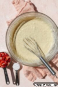 A bowl of waffle batter with strawberries and extra flour in measuring cups on the side.