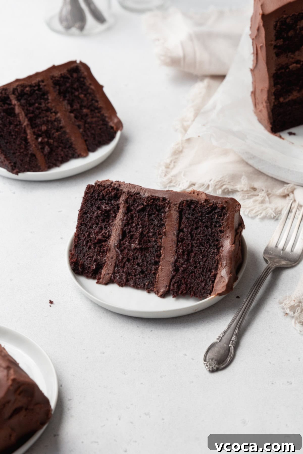 A slice of gluten-free chocolate cake on a small white plate with a silver fork next to it, and more cake slices around.