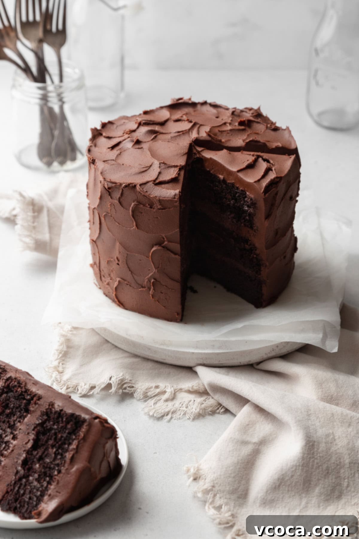 A frosted chocolate cake with a slice cut out, and another slice on a plate in front.