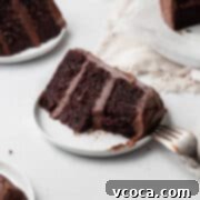 A bitten slice of gluten free chocolate cake with chocolate frosting on a small white plate.