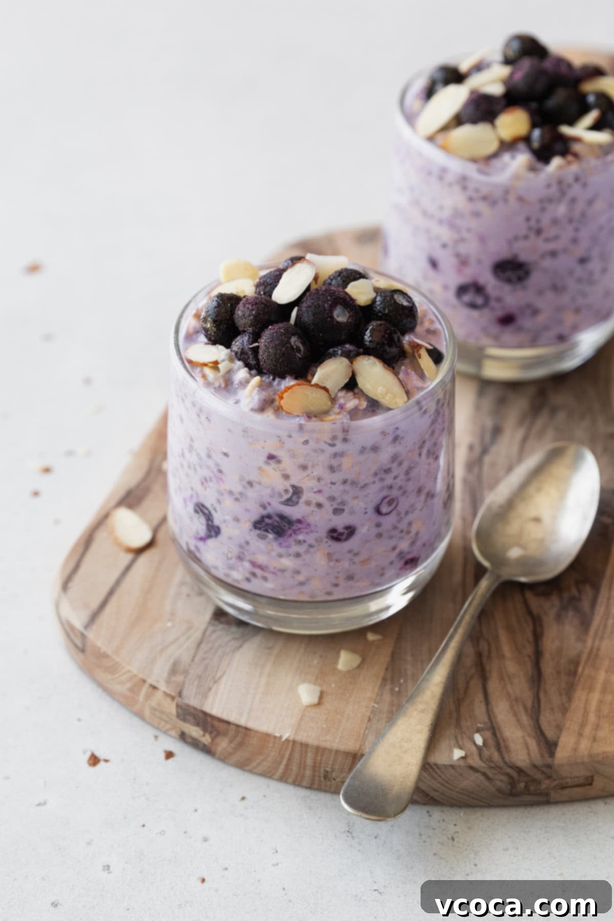 Effortless Blueberry Overnight Oats 2 Two glass jars of creamy blueberry overnight oats on a rustic wooden board with a spoon, ready for a healthy breakfast.