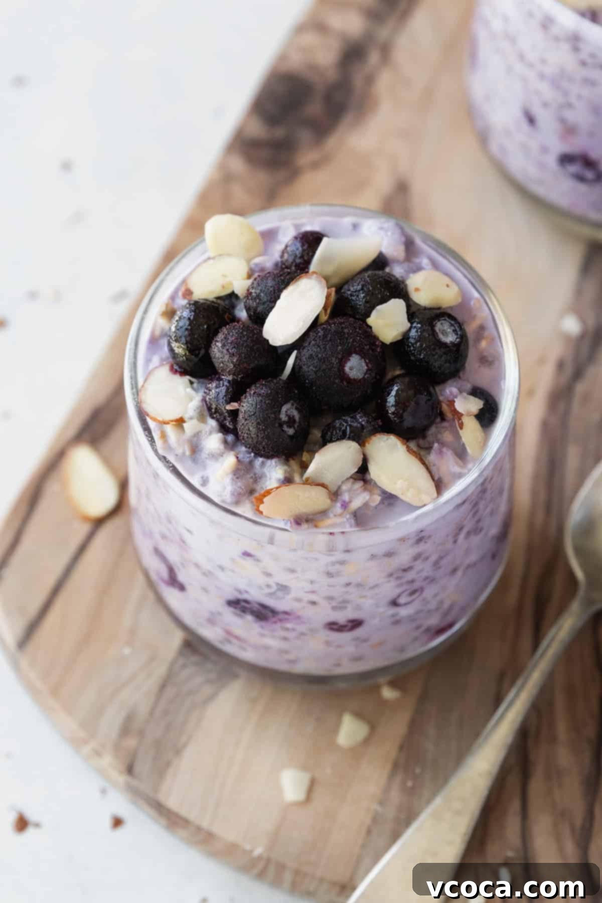 Effortless Blueberry Overnight Oats 6 A close-up shot of frozen blueberries and perfectly sliced almonds beautifully arranged on top of a glass jar of creamy blueberry overnight oats.