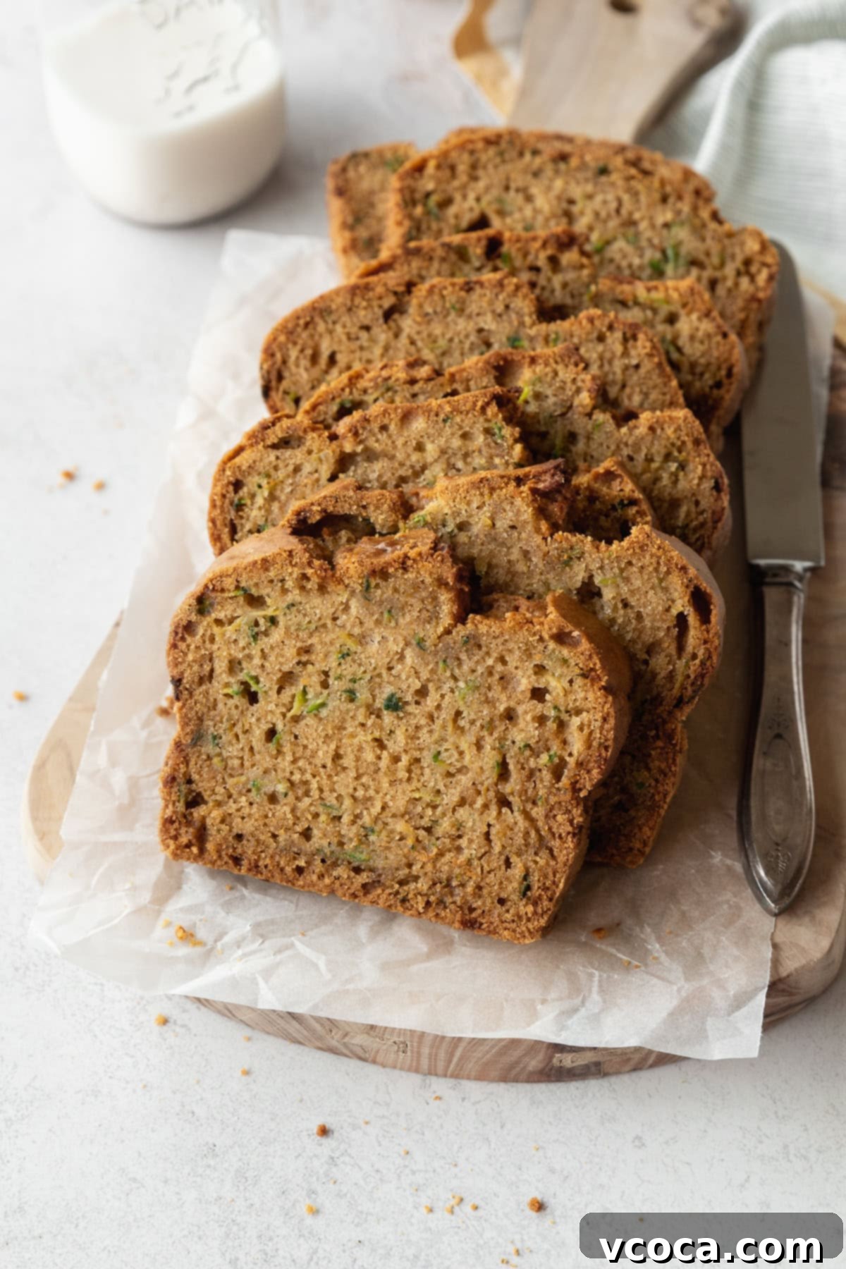 Gluten Free Zucchini Bread Delights 2 Slices of perfectly baked gluten free zucchini bread on a parchment lined wooden board, with a silver knife beside it, ready to be enjoyed.
