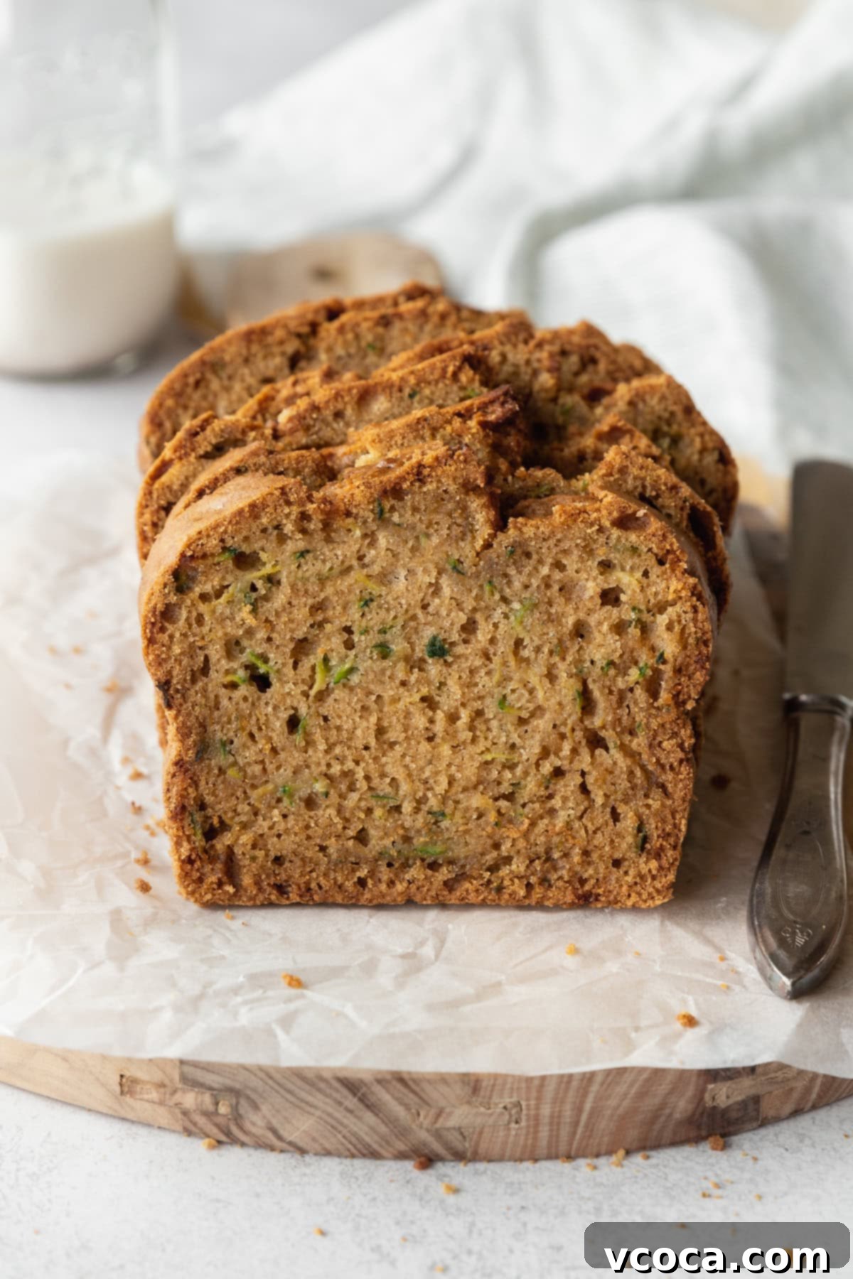 Gluten Free Zucchini Bread Delights 3 A beautifully sliced gluten-free zucchini loaf on a piece of parchment paper, with a bottle of milk in the background, inviting a delicious snack.