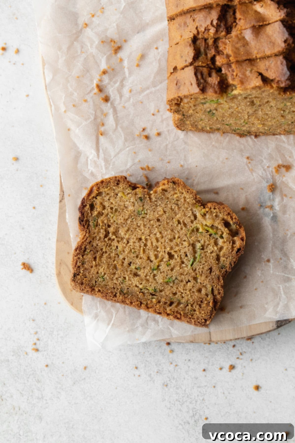Gluten Free Zucchini Bread Delights 8 A delectable slice of gluten-free zucchini bread on a parchment-lined wooden board, with more inviting slices to the side, ready to be enjoyed.