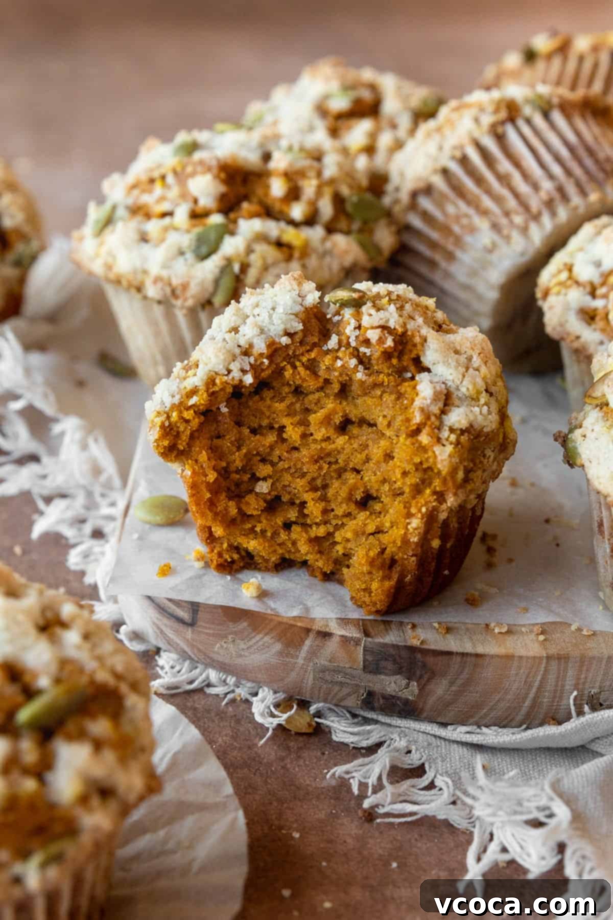 A gluten-free pumpkin muffin with a bite taken out, with more muffins around it.