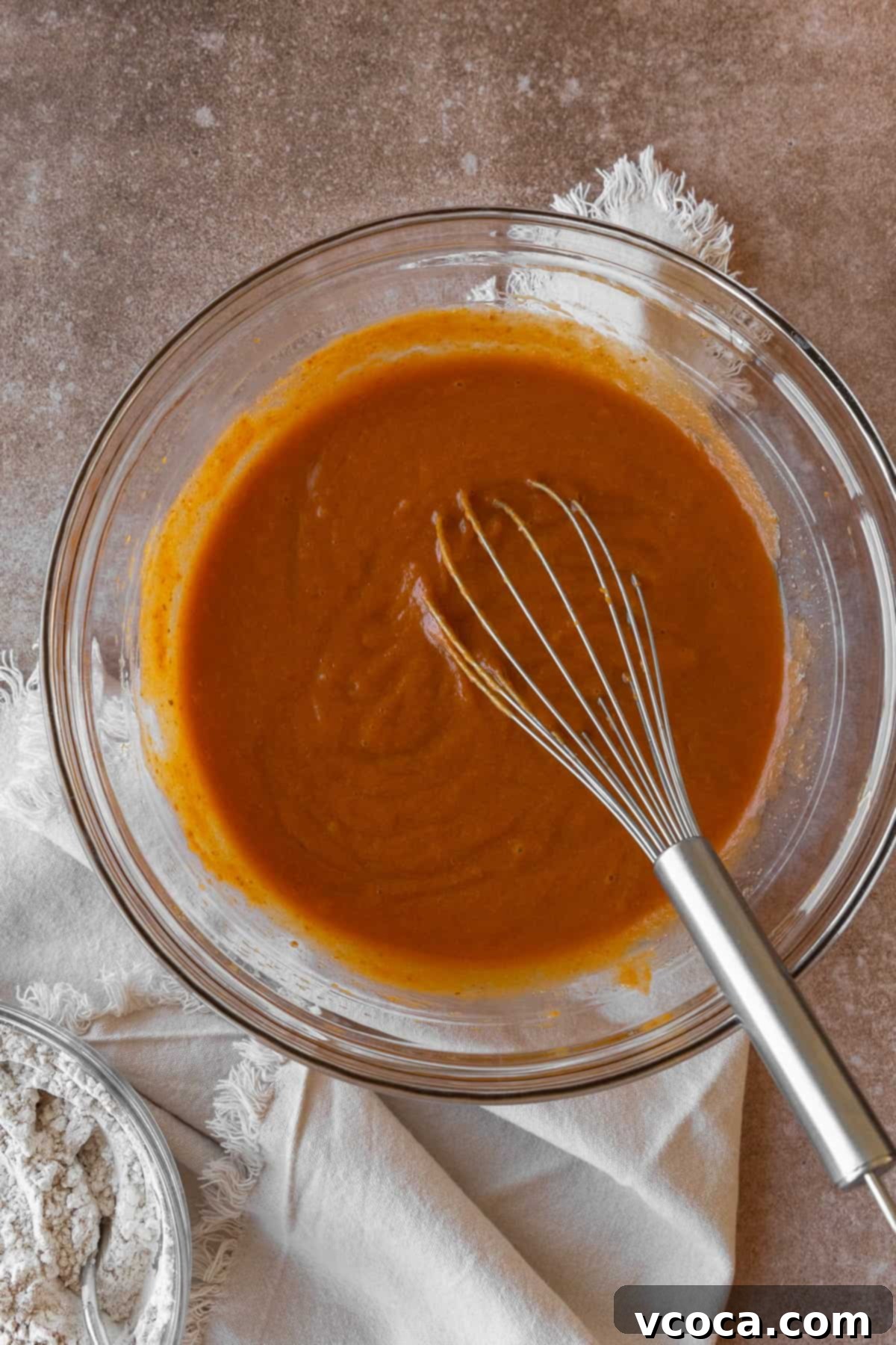 Wet ingredients for pumpkin muffins in a glass bowl with a wire whisk.