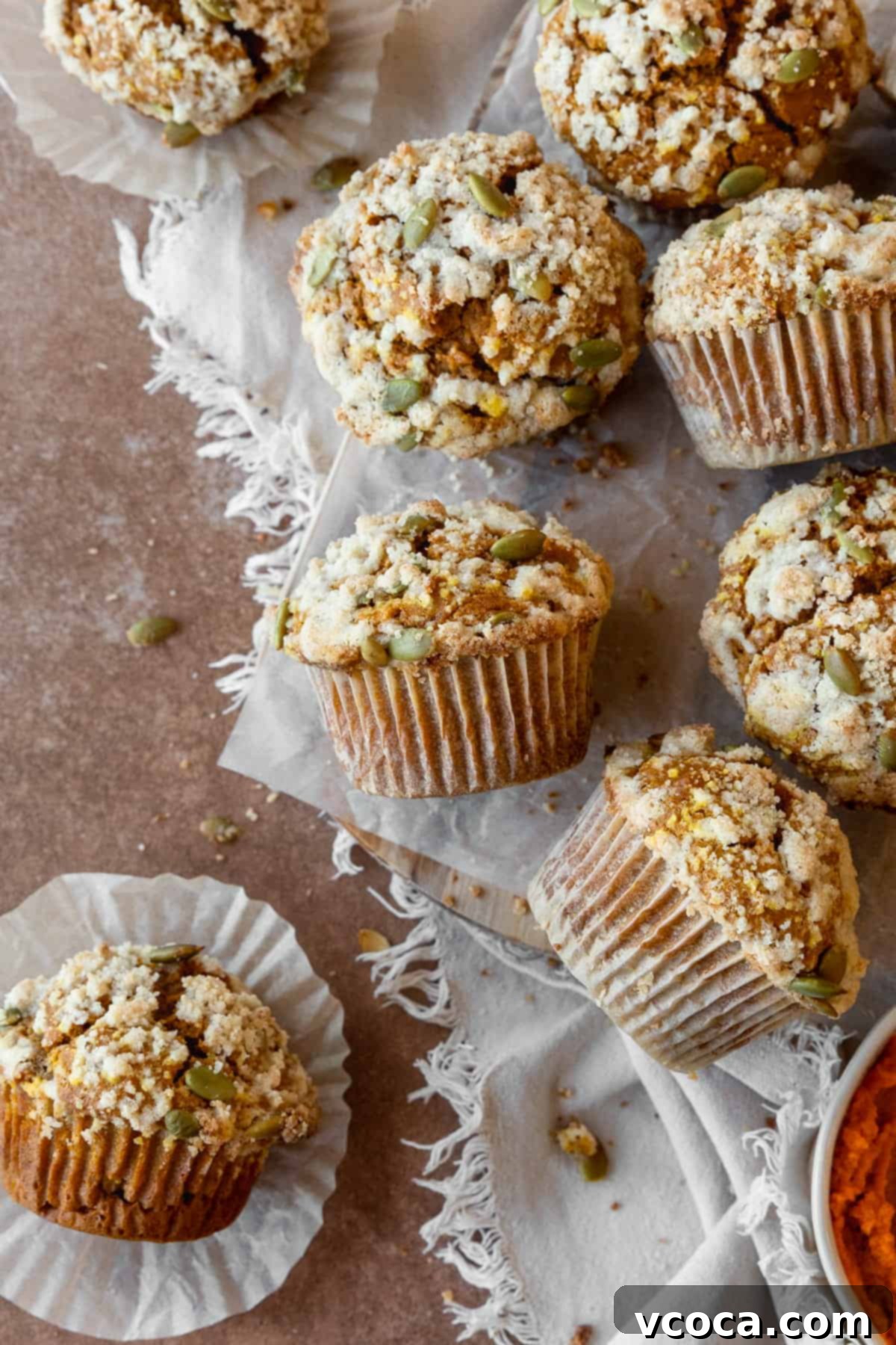 Gluten free pumpkin muffins with streusel scattered on a piece of parchment paper, with some on the side.