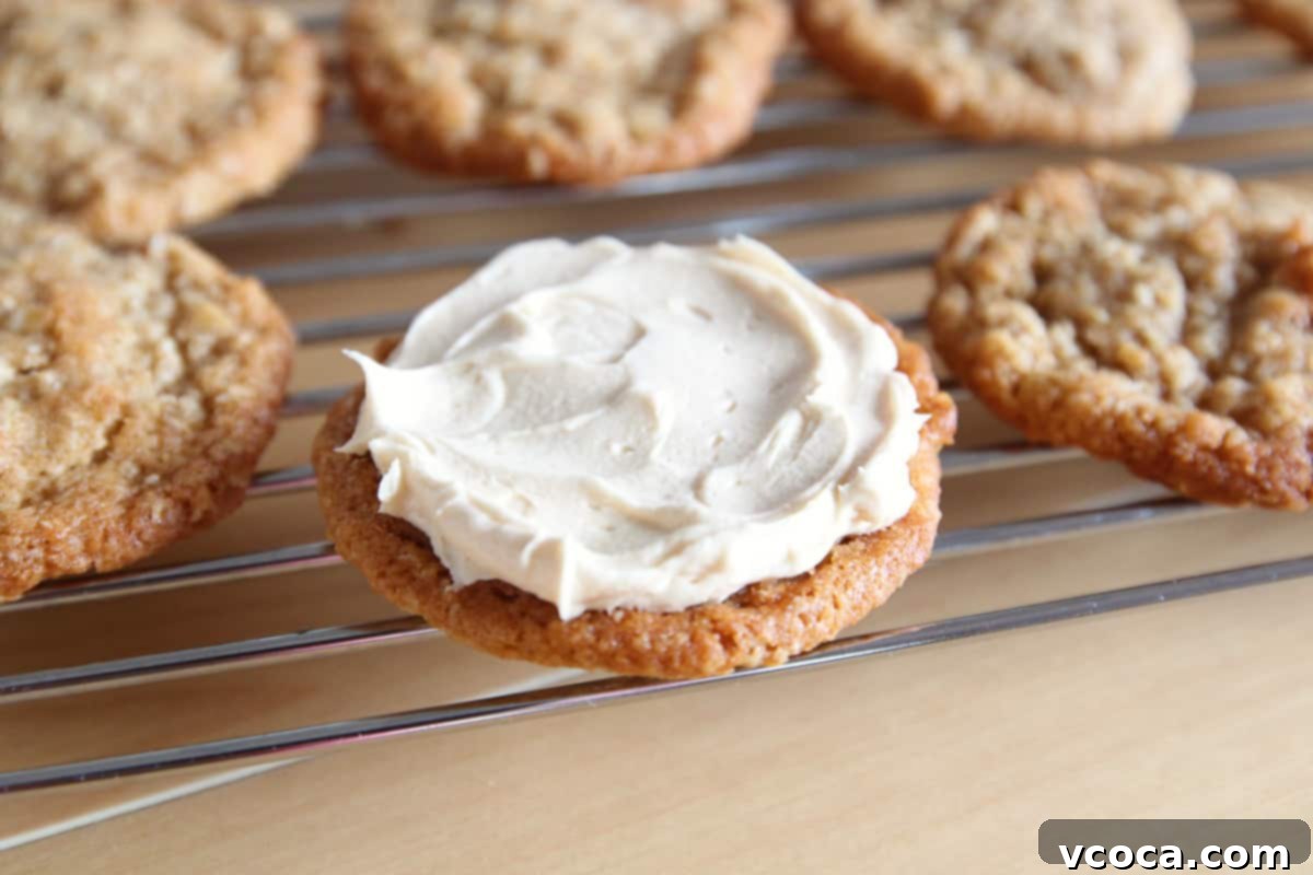 Scrumptious Chewy Coconut Oatmeal Cookie Sandwiches 4 An oatmeal cookie on a wire rack with some buttercream frosting spread on top.