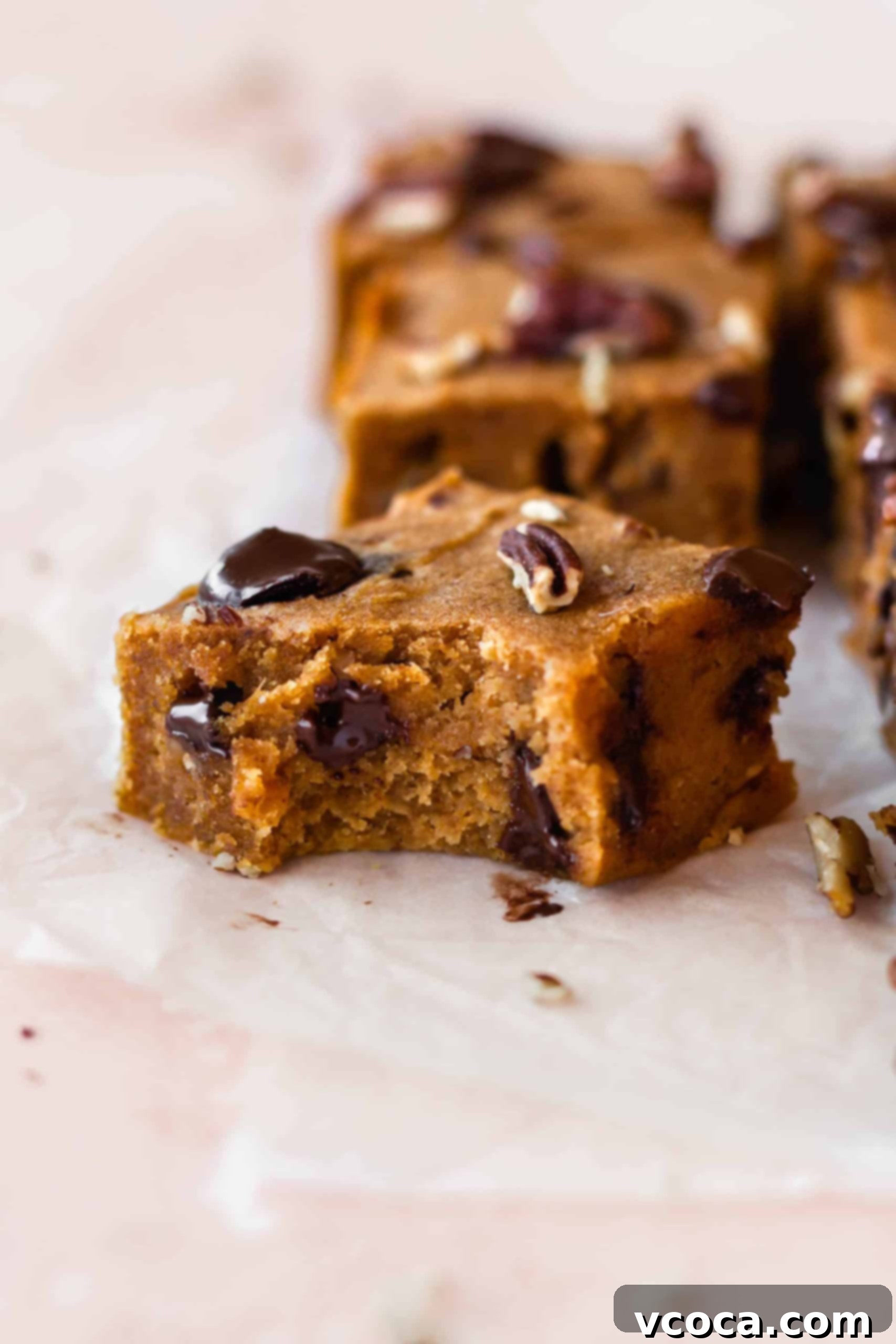 A hand reaching for a pumpkin bar with a bite taken out, showing its rich texture.