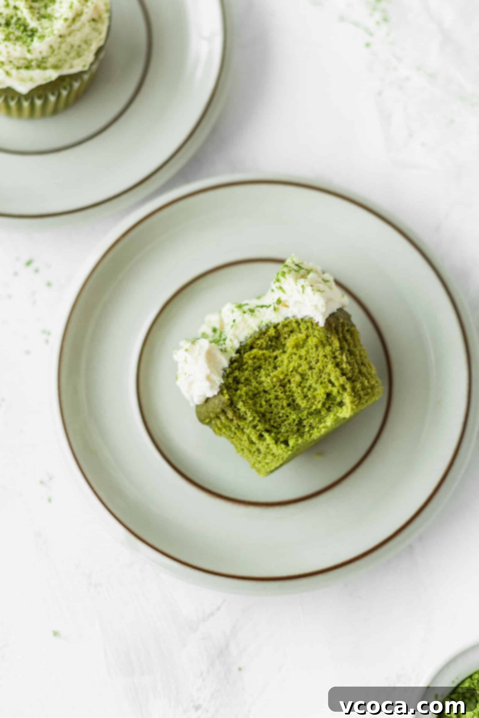 Half-eaten fluffy matcha cupcake with white chocolate frosting on a plate
