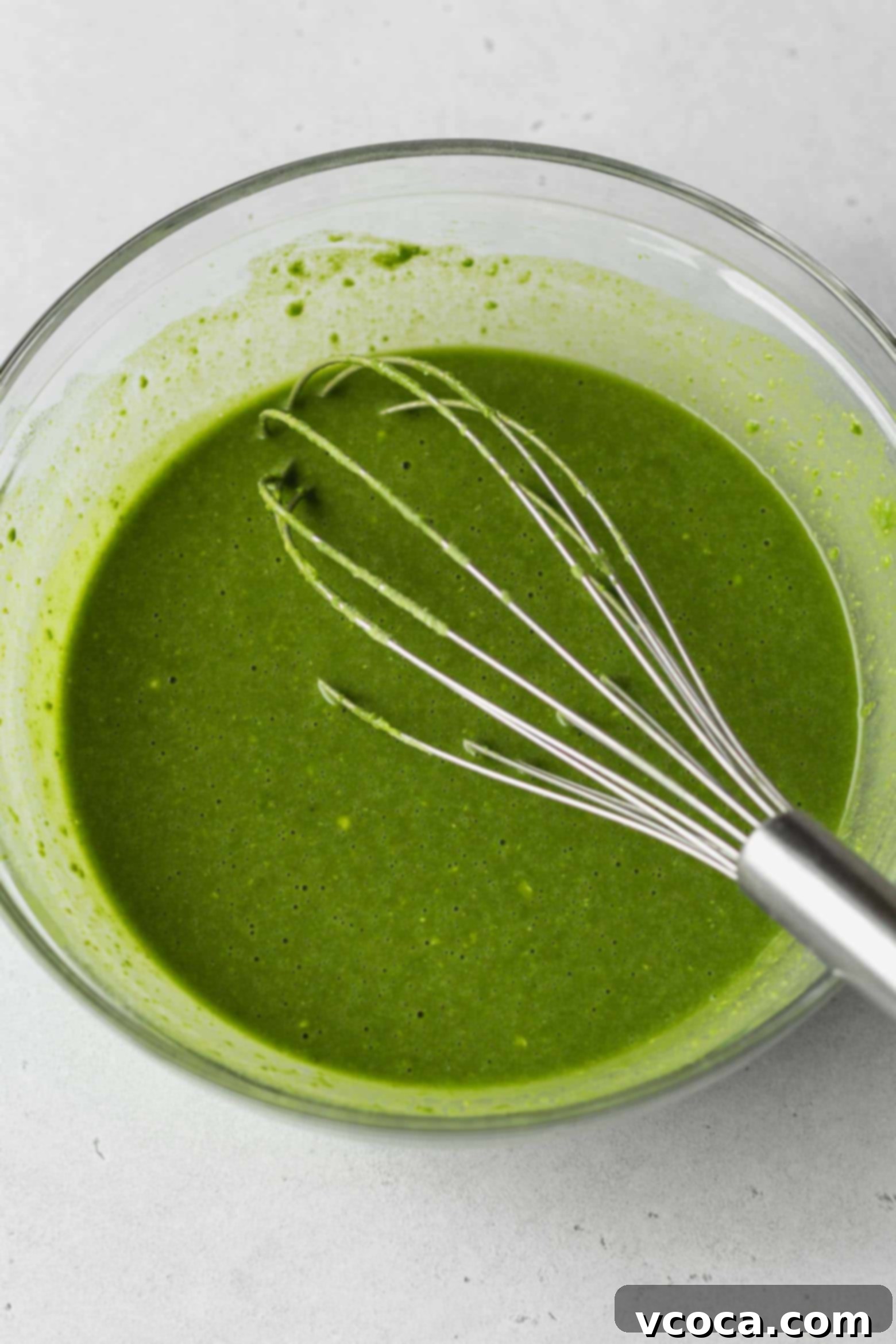 Bowl of matcha cake batter with a whisk