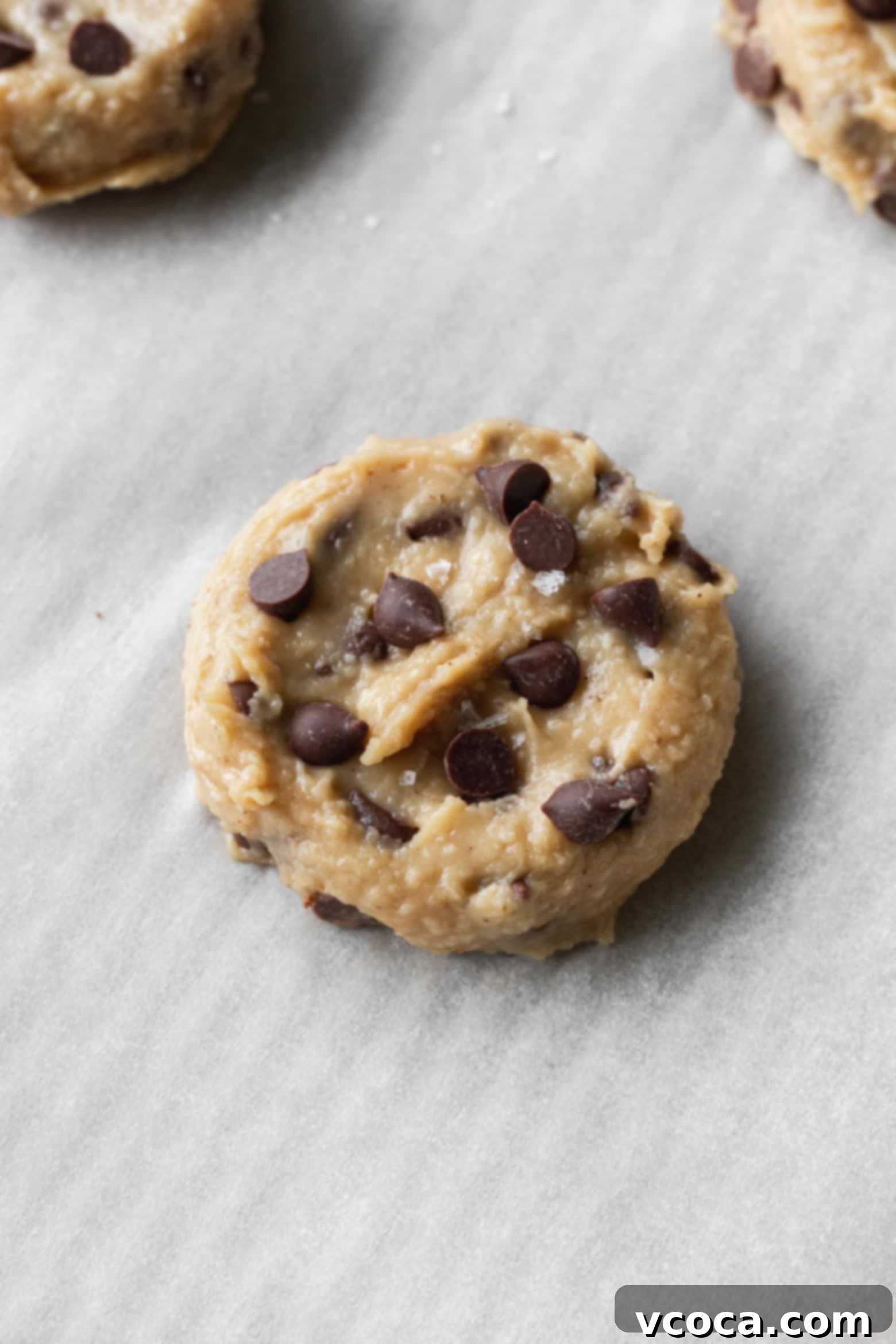 Close-up of chickpea cookie dough, flattened, with chocolate chips and a sprinkle of flaky sea salt on top, ready for baking.