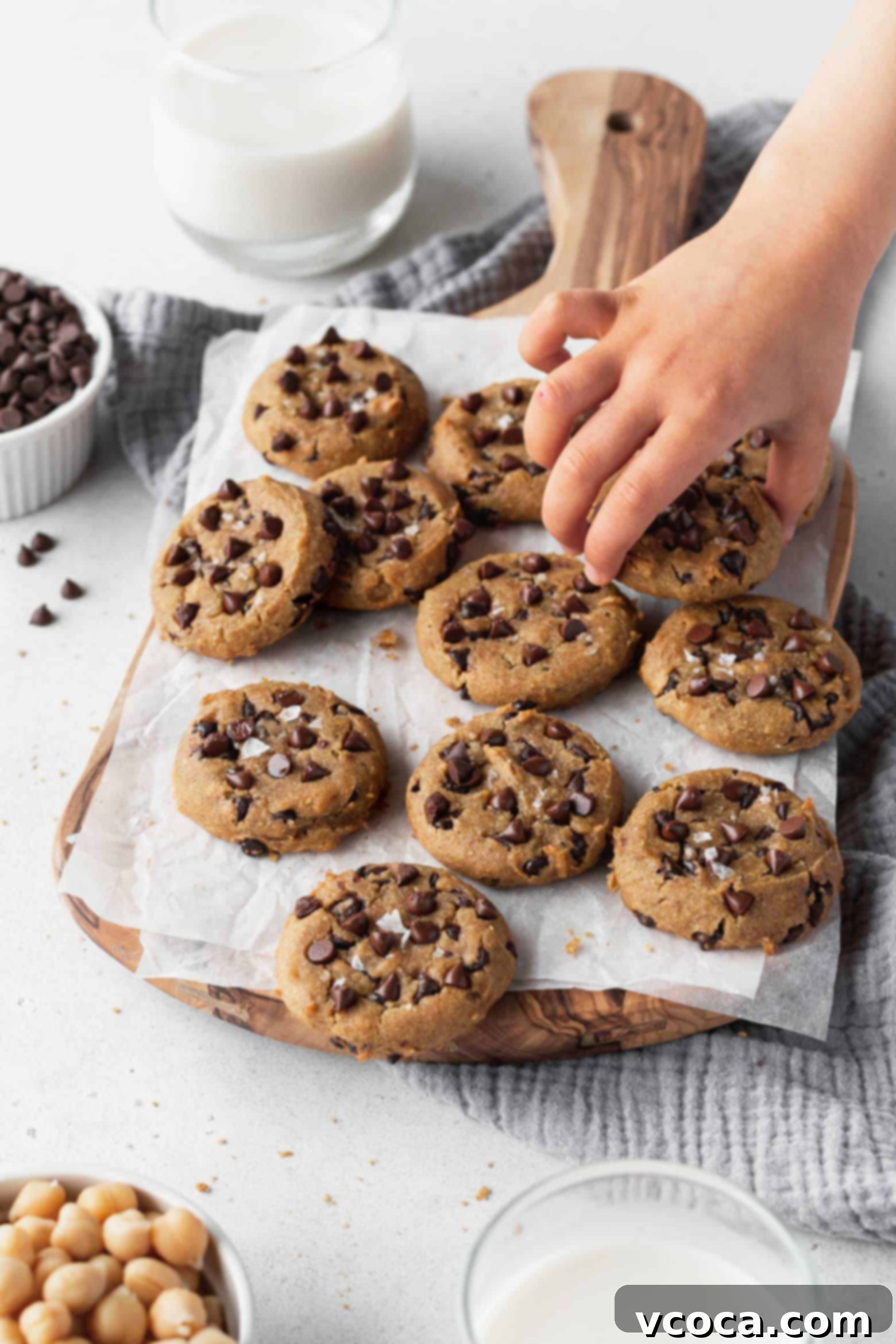 A child's hand reaching eagerly to grab a delicious chocolate chip chickpea cookie from a plate, symbolizing their irresistible appeal.