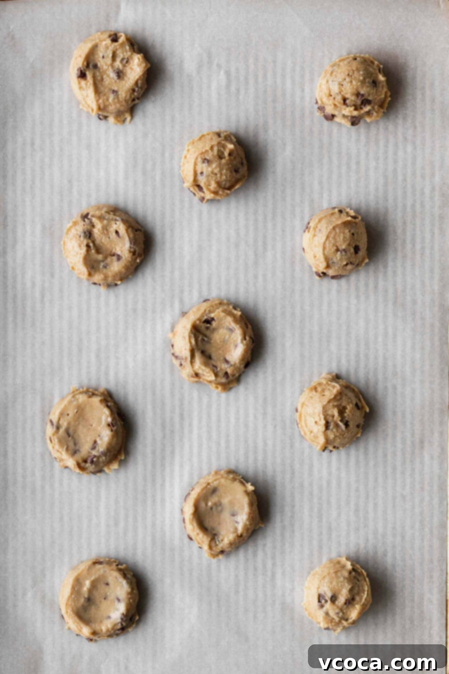 Unbaked chickpea cookie dough balls placed evenly on a parchment-lined baking sheet, ready for the oven.