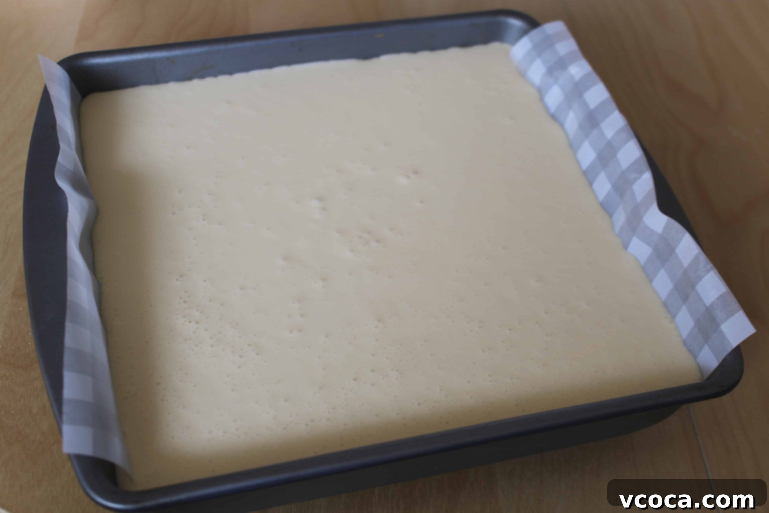 Cheesecake crust pressed into a parchment-lined square pan, ready for filling