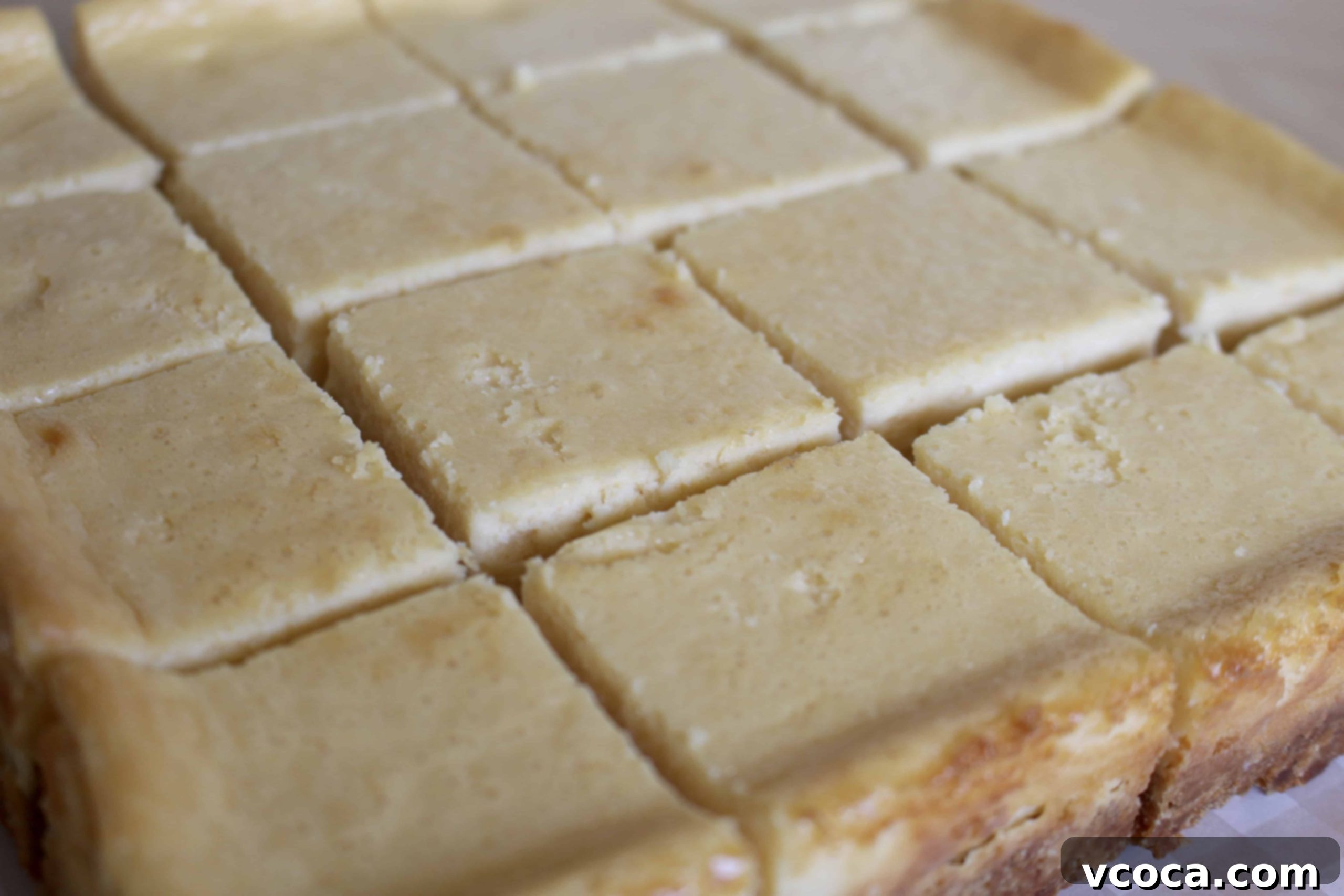 Cheesecake bars being carefully removed from the pan using parchment paper handles