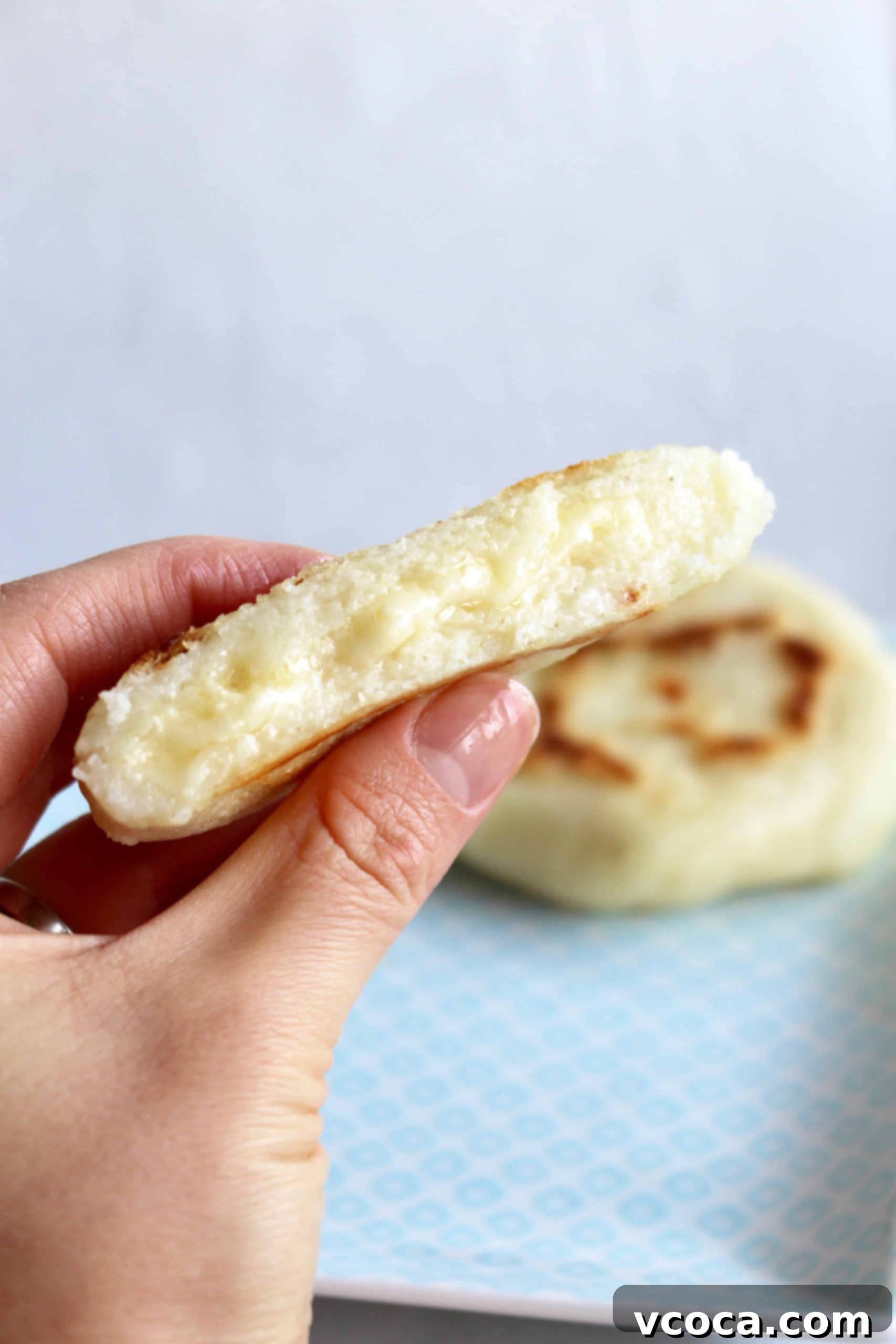 A hand holds a perfectly cooked arepa, sliced open to reveal melty, golden cheese stuffing. The arepa has a beautifully crispy exterior.