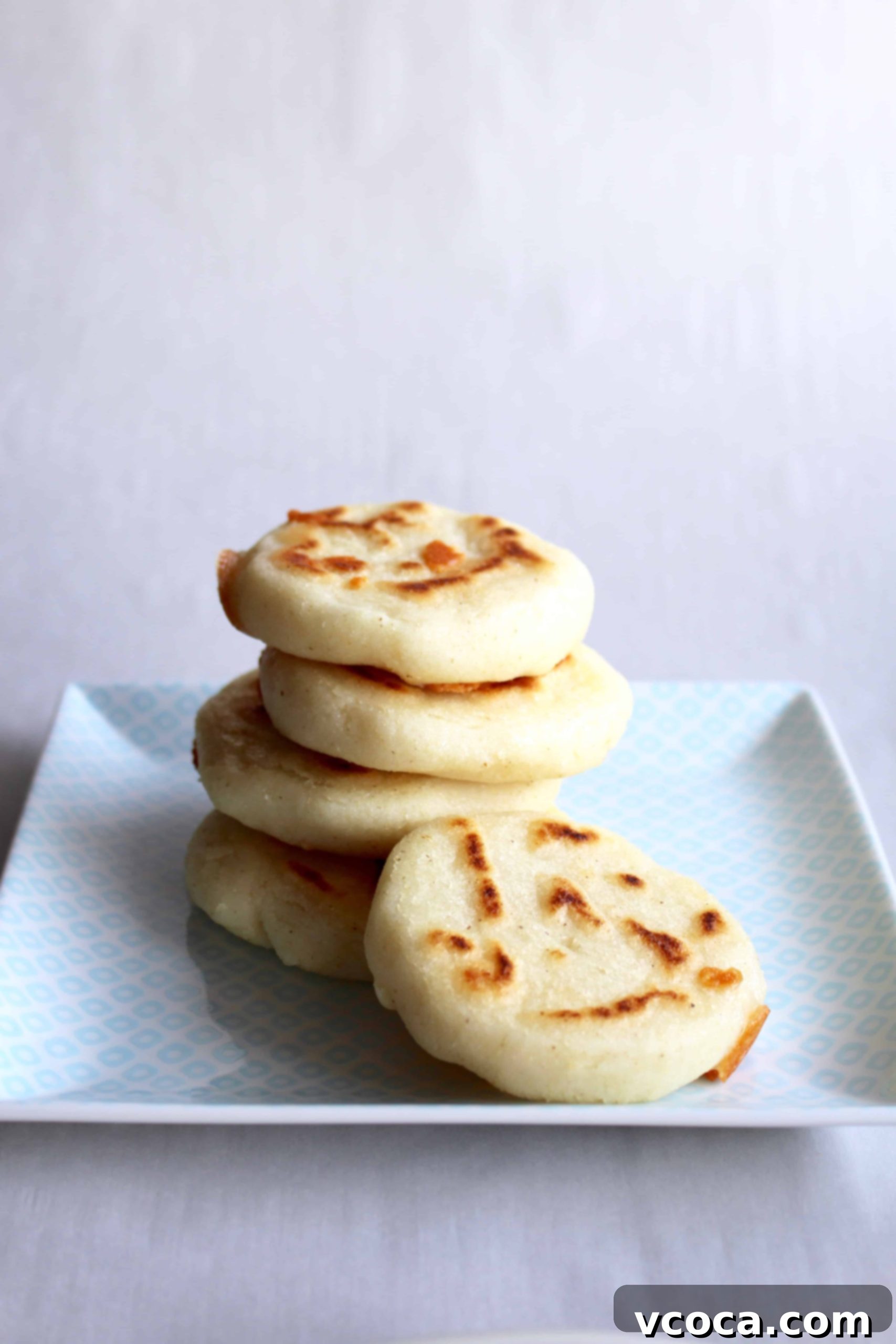 A perfectly arranged stack of golden-brown arepas rests on a square white plate, ready to be filled and served.