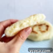 A hand holding a warm, golden-brown arepa, sliced open to reveal melty cheese inside.