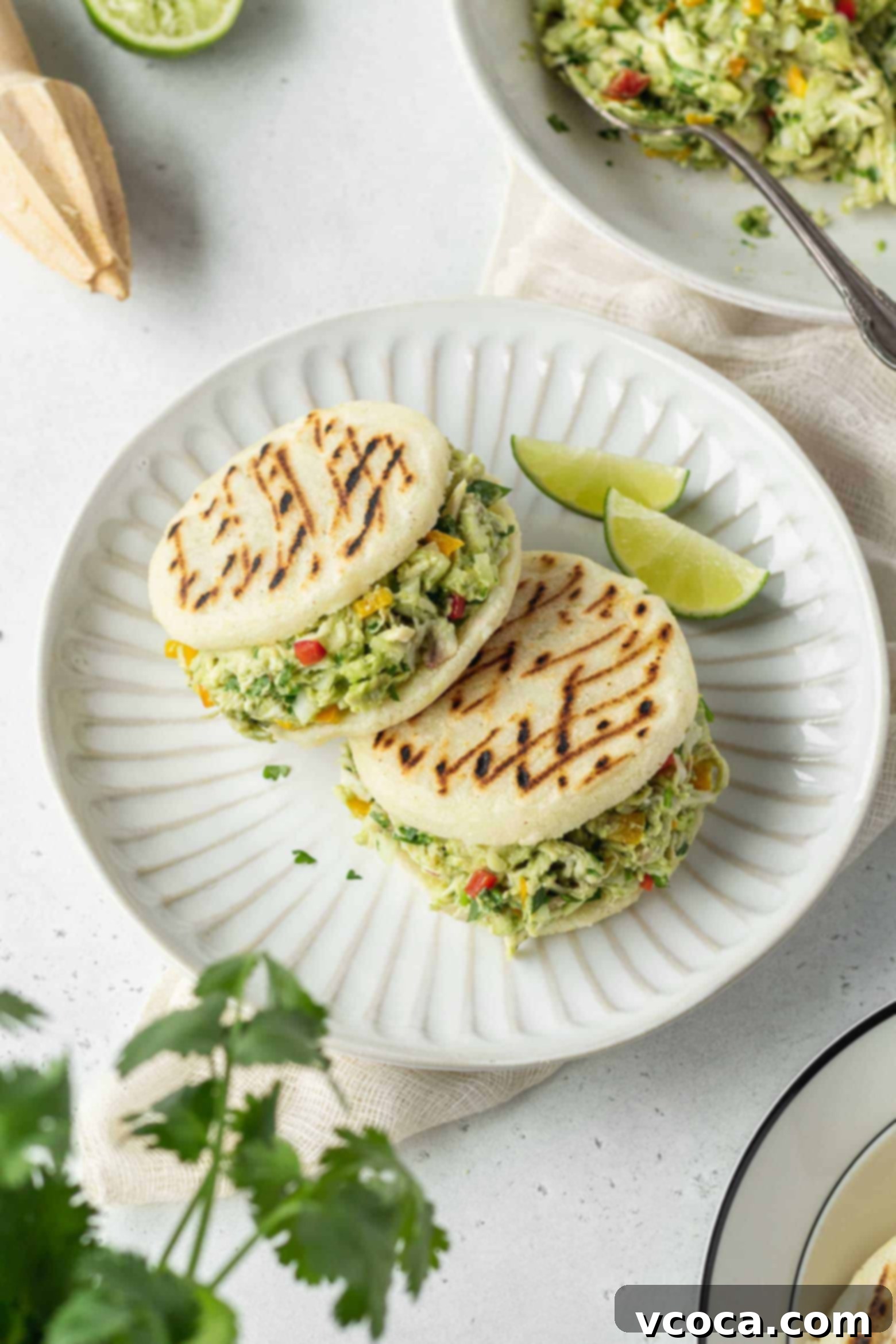 Reina Pepiada Venezuelan Arepas 2 Two Reina Pepiada arepas on a plate with lime wedges, showcasing the delicious chicken and avocado filling