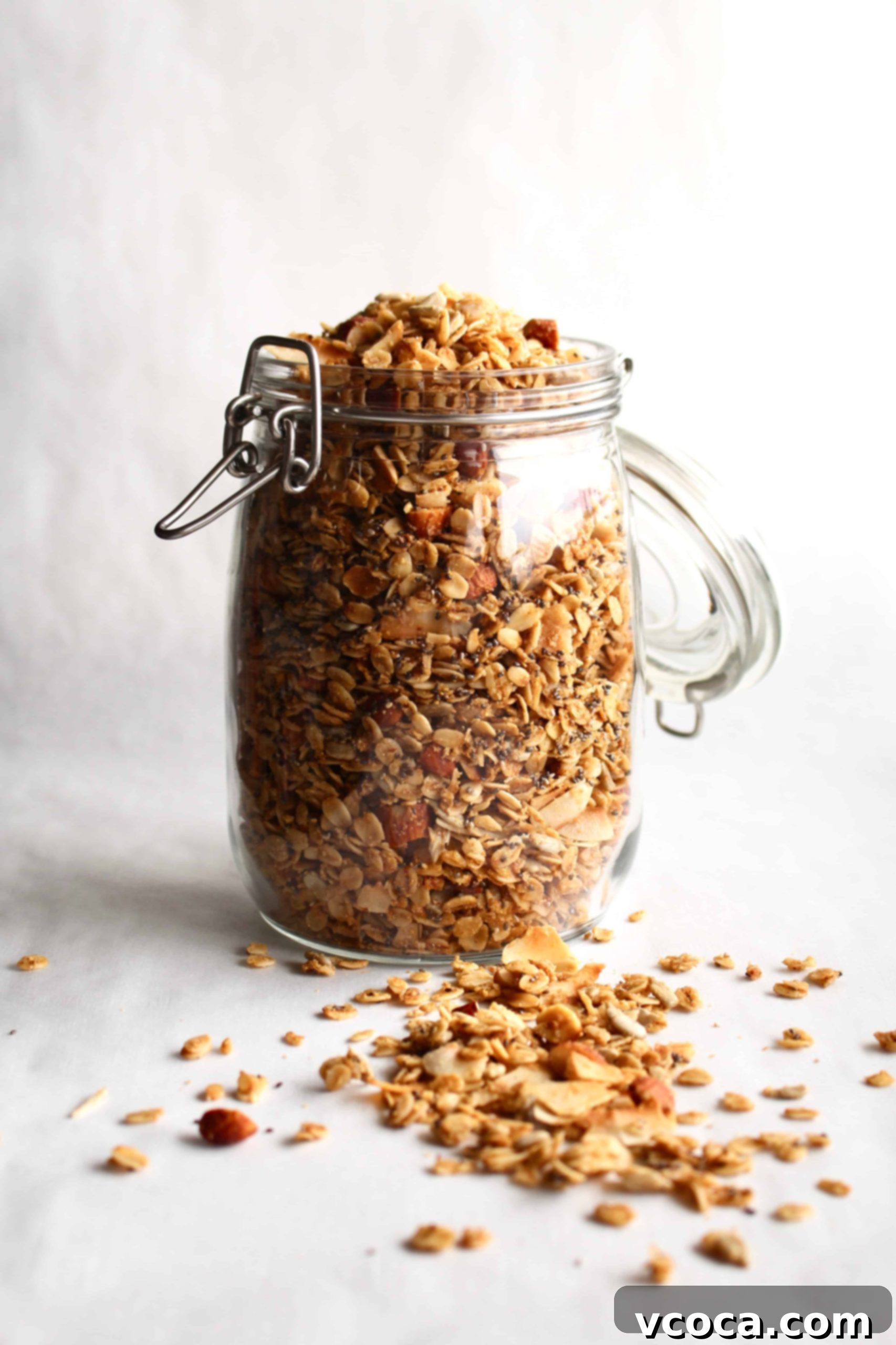 Seriously Delicious Gluten-Free Granola 2 A glass jar of gluten-free granola on a white surface, with some granola spilled in front of the jar.