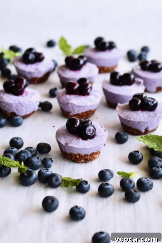 Effortless Blueberry Cheesecake Treats 2 Blueberry cheesecake bites scattered on a white surface with mint leaves and fresh blueberries, highlighting their vibrant color and fresh appeal.