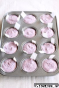 Mini muffin pan wells filled with vibrant purple vegan blueberry cheesecake batter, ready for chilling.