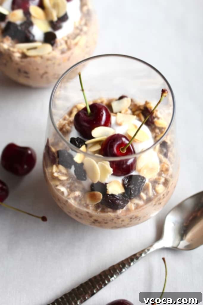 A vibrant and appealing glass of cherry almond overnight oats, beautifully garnished with fresh and dried tart cherries, toasted almonds, and a touch of creamy yogurt, making for a perfect, healthy, and easy breakfast or snack.