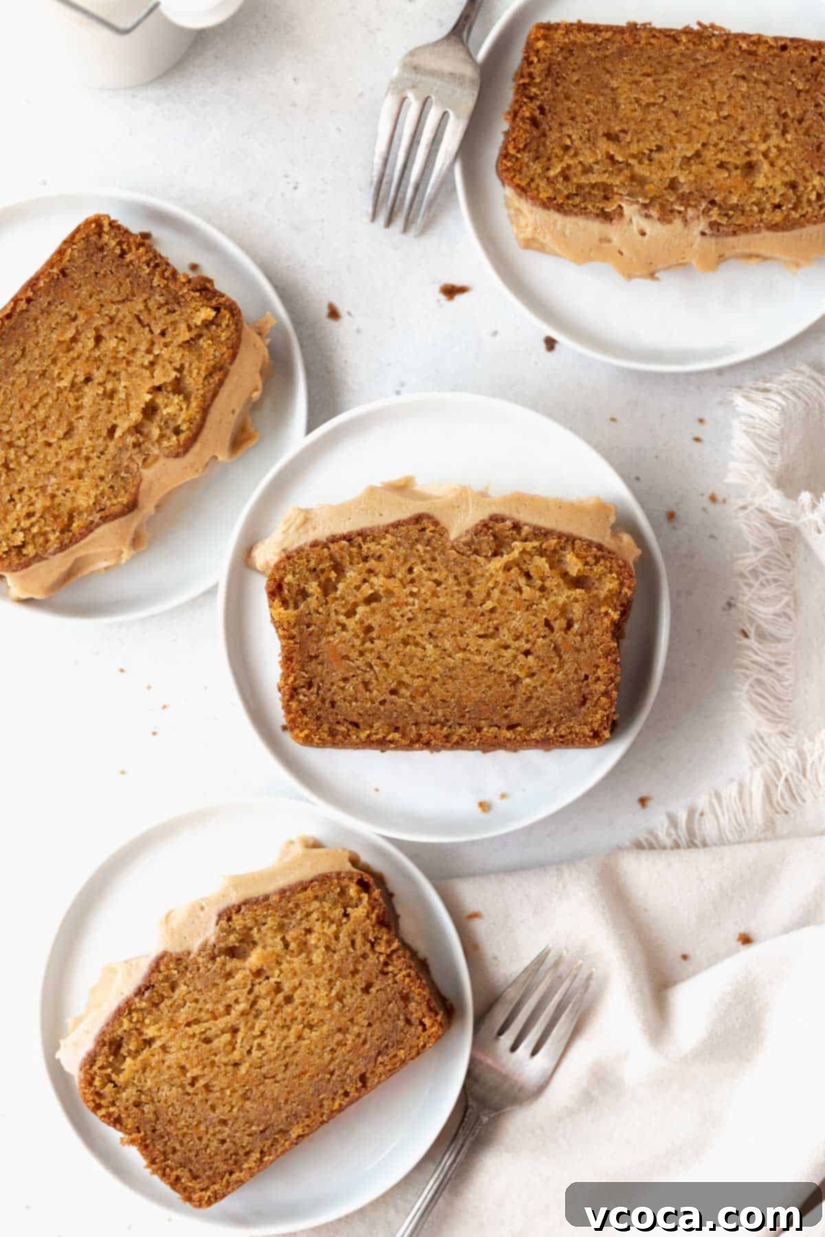 Spiced Sweet Potato Cake with Cashew Frosting 19 Overhead shot of sweet potato cake slices on white dessert plates with silver forks on a white surface.